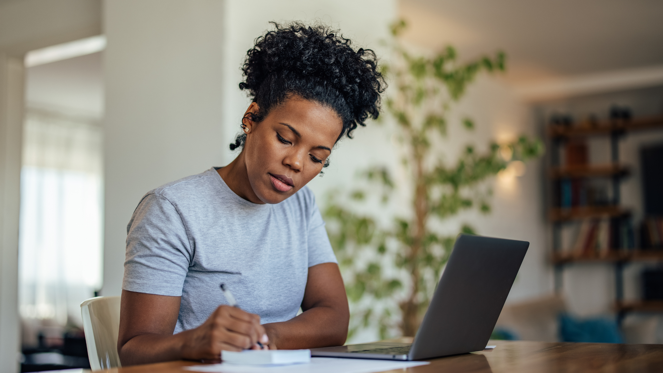 A focused woman writing notes at a desk with a laptop, symbolizing the dedication and planning required to succeed in ethical online money-making ventures