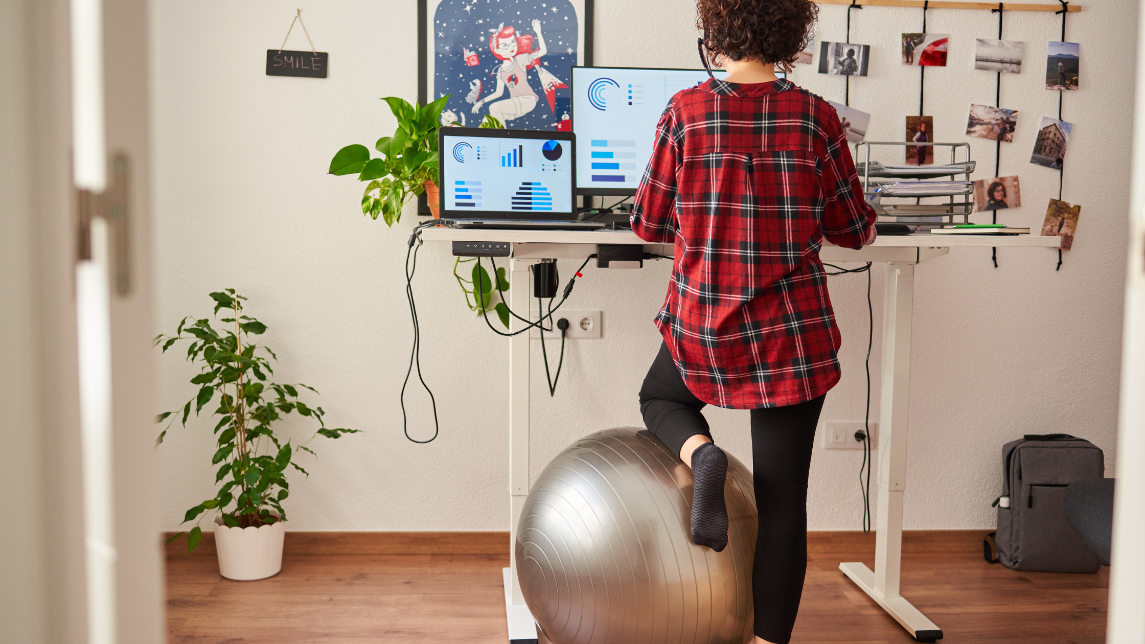 A person working from home, balancing on an exercise ball at a standing desk with multiple screens displaying charts and graphs, illustrating the flexible and active lifestyle of making money online through ethical methods